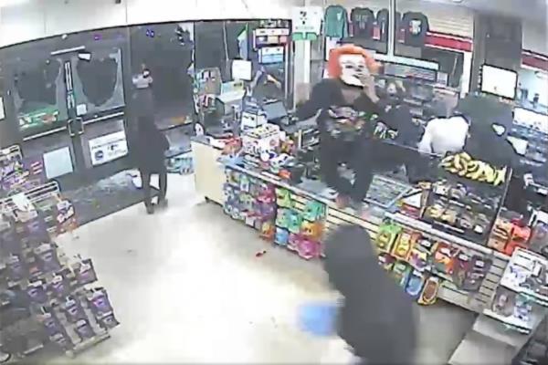 Surveillance footage showing a man dressed in a clown mask jumping over the counter as others ransack the store.